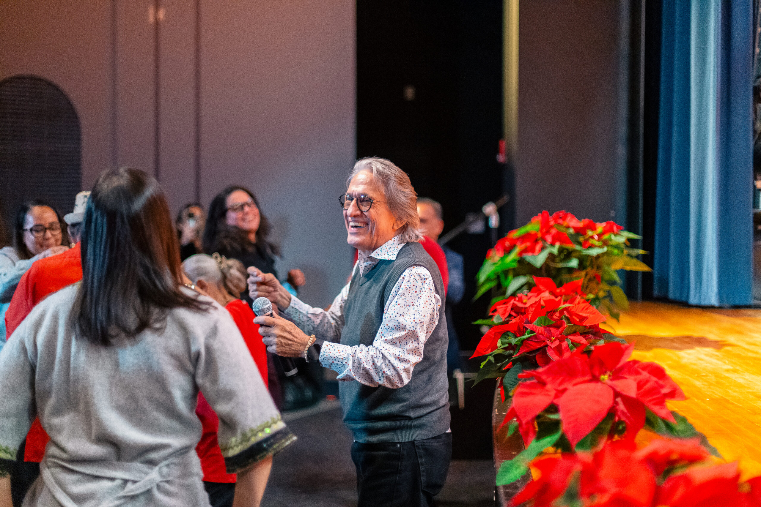 A person holding a microphone in front of a stage that's lined with red flowers